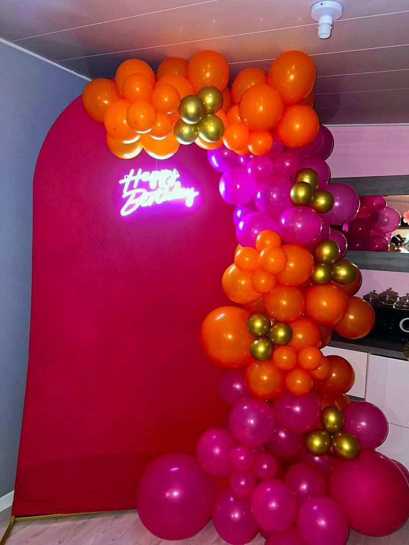 Arche fuchsia avec néon Happy Birthday et guirlande de ballons orange, fuchsia et dorés
